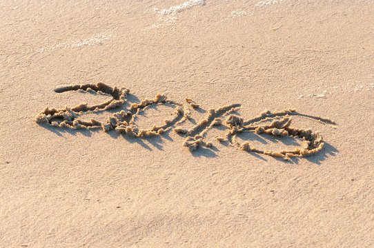 Year 2016 written in the Sand on a Beach against sunset
