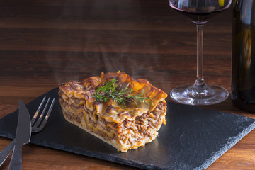 fresh hot steaming lasagna pasta served on wooden table and slate plate