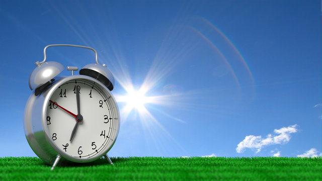 Retro alarm clock closeup on grass with blue sky and sun shining.