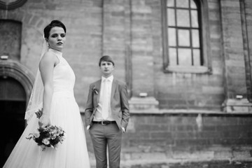 Fototapeta na wymiar Beautiful brunette bride posing with bouquet, church & groom bac