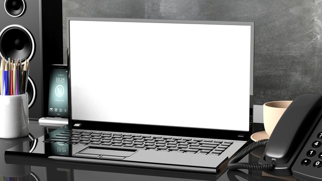 Blank white laptop screen set on office desk with various objects
