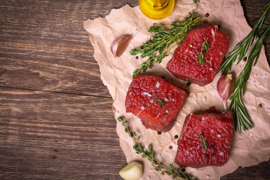 Raw beef steak with rosemary, thyme and garlic on wooden background