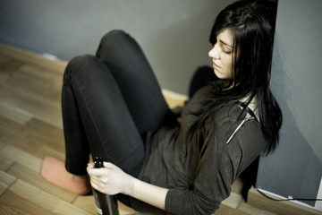 Lonely woman sitting on ground  at home holding bottle of wine