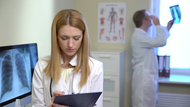 Young female doctor working with medical notes and male doctor looking x-ray on background. 4k