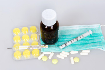 Tablets, cough syrup with a measured syringe, dressing on the face, a thermometer on a white background. Proceeds from the common cold and flu.