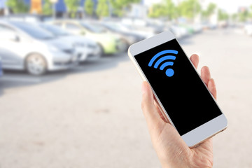 smartphone in hand with wi-fi icon on blurred car parking area