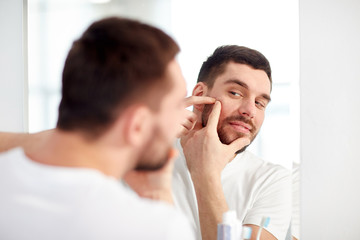 man squeezing pimple at bathroom mirror