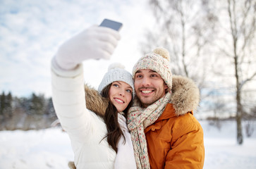 Fototapeta premium happy couple taking selfie by smartphone in winter