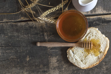 Honey in a jar, bread, wheat and milk on wood table.