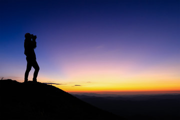 silhouette of woman taking photograph on the top of mountain and enjoy colourful sky