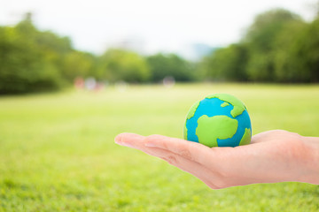 human hands holding planet or earth over blurred green garden nature background. Ecology concept.