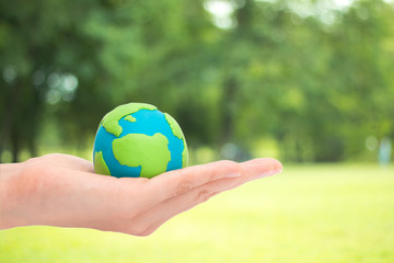 human hands holding planet or earth over blurred green garden nature background. Ecology concept.
