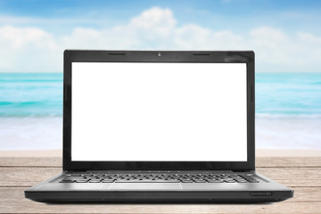 Fototapeta premium Laptop with blank screen on wooden table blurred sea and beach background