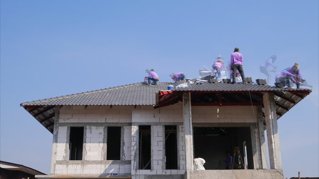 unidentified construction workers installing roof tiles for home building 