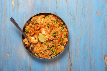 Traditional spanish paella dish with seafood, peas, rice and chicken over grunge blue background. Top view. Selective focus