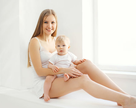 Happy smiling mother and baby at home in white room near window