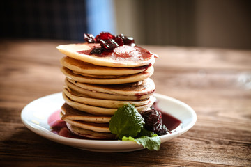 stack of pancakes on a white plate with cherry jam, mint leaves,