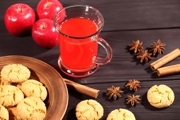 Composition with a large cup of hot drink, which stands on a rustic vintage black table next to a plate of homemade cookies, red apples, star anise and cinnamon sticks. Selective focus