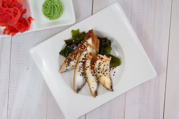 Eel sashimi with ginger and wasabi on a white plate over wooden background