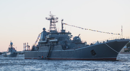 Grey modern battleship warship sailing in still water against summer sky with one more warship in the background