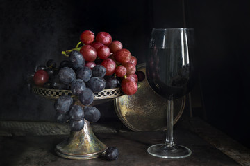 Variety of grapes and a glass of red wine on dark background - vintage, moody style