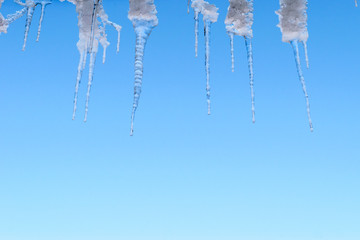 Spring thaw, ice icicles on blue sky background.