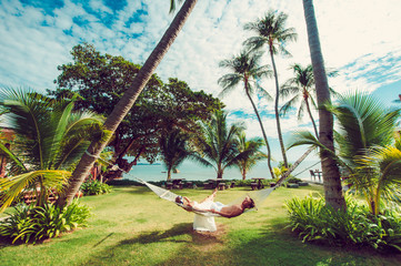 On a hammock in the tropics . Relaxing in hammock on tropical beach .