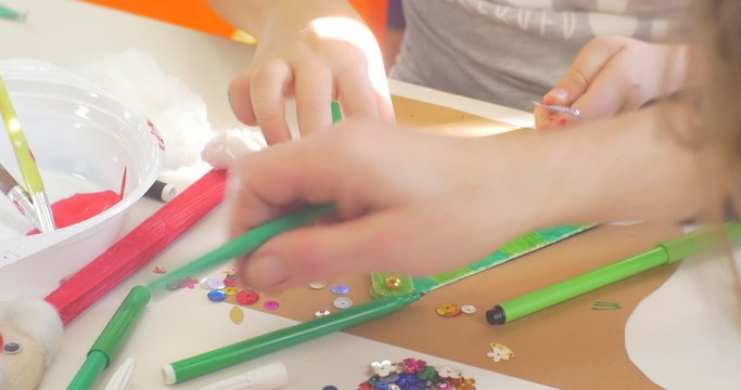 Kids Hands Are Decorating a Triangle With Beads and Sequins Hands Close Up Kids are Sitting at the Table Colorful Markers are on the Table