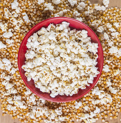 Bowl of popcorn snacks, on wooden table with uncooked corn.