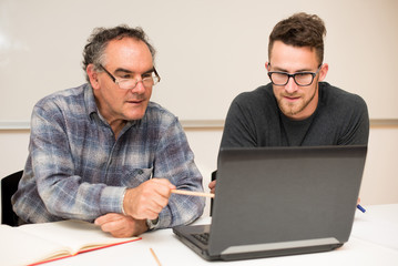 Young man teaching eldery man of usage of computer. Intergenerat