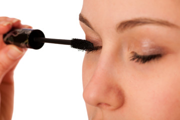 Woman applying black mascara on eyelashes, doing makeup.