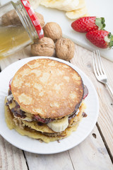 pancakes with banana, nuts and strawberry on wooden background