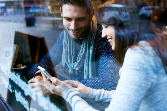 Beautiful young couple using mobile phone in restaurant.