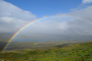 Fototapeta na wymiar Clouds, rainbow and sunshine over valley in subarctic mountains, Swedish Lapland
