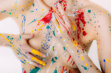 Colorful young woman in paint with hands on breasts on white background