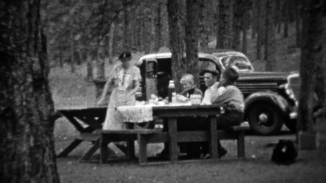 1935: Family picnic in pine tree forest at new black Plymouth car.