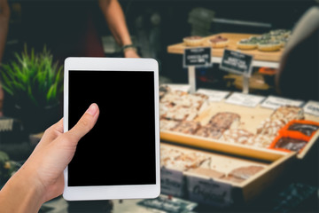 Hands are holding touch screen White Tablet Computer on blurred shopping super market background.