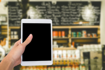 Hands are holding touch screen White Tablet Computer on blurred shopping super market background.