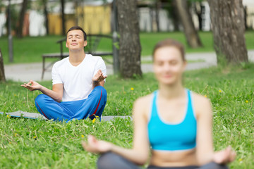 Fototapeta premium Young couple meditating on green grass