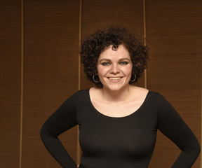 Young woman in brown scoop-neck blouse standing before bamboo shades