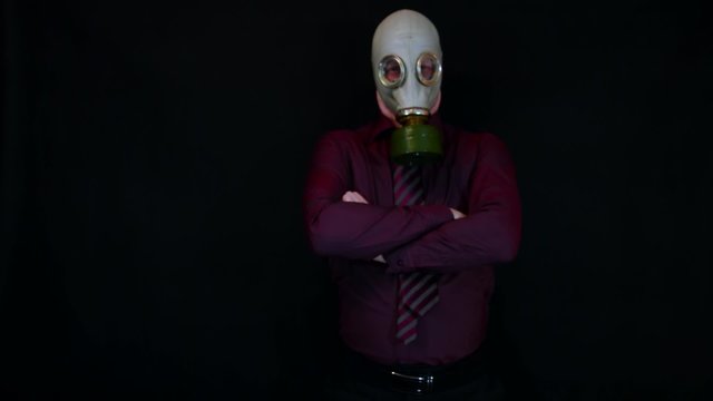 businessman on a black background in a gas mask with displeasure crossed his arms and leans