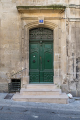 Fototapeta na wymiar Od gate with ornaments and closed green doors in an old building in a street in Arles, France on a sunny day in the summer