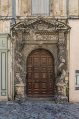  Very old, worn and dirty gate with ornaments and a closed wooden door in an old building in a street in Arles, France on a sunny day in the summer