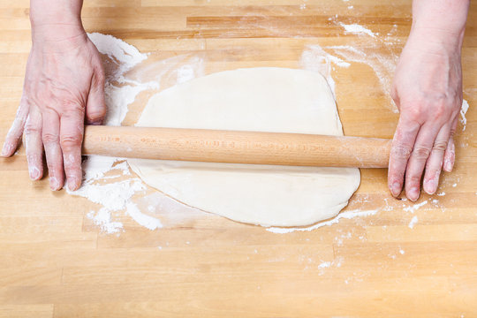 female hands roll out dough with rolling pin