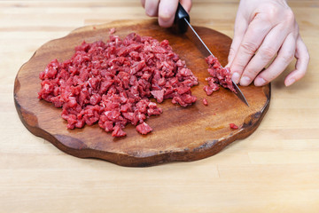 woman finely chops meat on cutting board