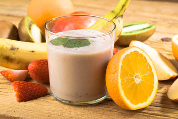 Natural banana smoothie surrounded by fruit on wooden base