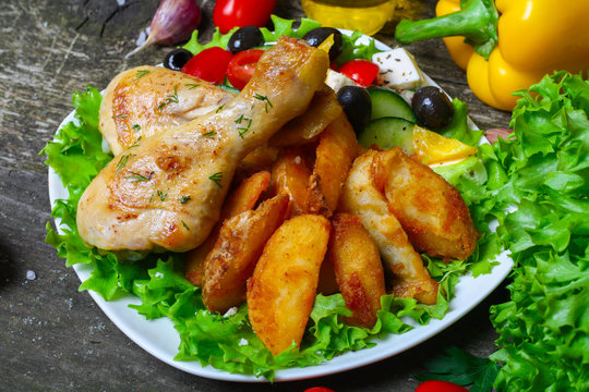 roasted chicken legs with potatoes with Greek salad on wooden background with vegetables
