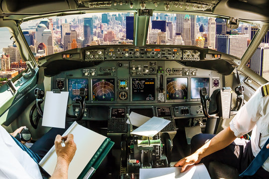 Cockpit and board of an airplane flying on New York skyline of United States of America.. Pilots arms and blank white papers for copy space
