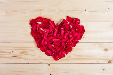 Heart by red roses petals on wooden board
