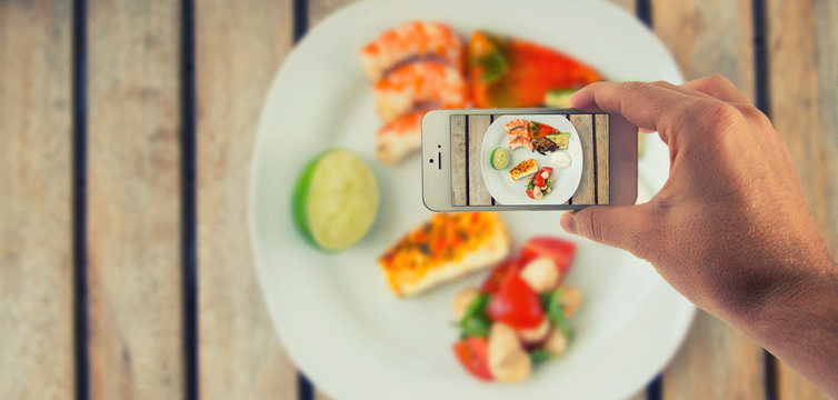 M&auml;nnliche Hand haltet ein wei&szlig;es Smartphone und fotografiert damit Essen